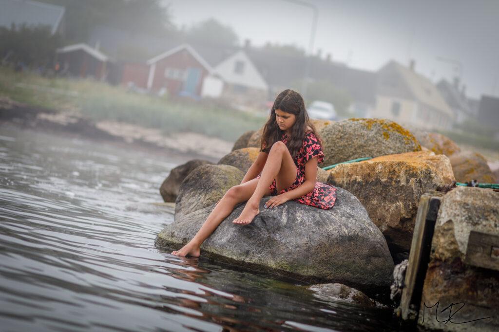 En flicka på en sten i en dimmig hamn